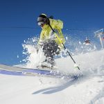 Professional skier dressed in bright yellow sportswear riding down the mountain slope in Georgia, Gudauri on sunny day
